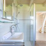 Badezimmer mit Dusche, Waschbecken und Spiegel. Durchgang zur Treppe.