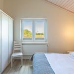 Schlafzimmer mit Bett, Kleiderschrank und Fenster mit Blick auf Grünfläche.