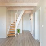 Hausflur mit Holztreppe, Holzboden und Deckenbalken. An der Wand hängt eine Lampe.
