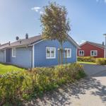 Blauer Ferienhaus mit Garten und Baum. Rote Häuser im Hintergrund.