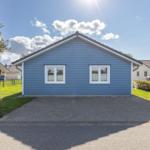 Blau gestrichenes Haus mit weißen Fenstern und gepflastertem Vorplatz.
