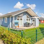 Blau gestrichenes Ferienhaus mit Terrasse, Garten und Sonnenliegen.
