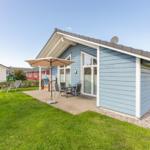 Blau gestrichenes Ferienhaus mit Terrasse, Sonnenschirm und Garten.