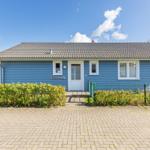 Blau gestrichenes Ferienhaus mit weißen Fenstern und Eingangstür. Vorgarten mit Hecke und gepflastertem Hof.