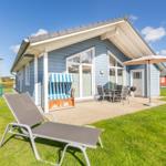Blauer Ferienhaus mit Terrasse, Liege und Sonnenschirm im Garten.