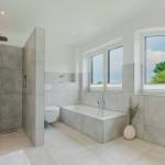 Badezimmer mit Dusche, Badewanne und großem Fenster mit Blick auf Grün.