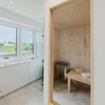 Sauna mit Holzwand und Bank. Fenster mit Blick auf Garten. Glaswand und Holztisch.