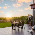 Terrasse mit Tisch, Stühlen, Grill und Liege im Sonnenuntergang.