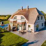 Modernes Haus mit Strohdach, Terrasse und Pool im Grünen.
