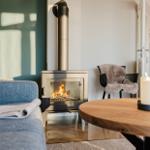 Ein Kamin mit brennendem Holz, ein Sofa und ein runder Tisch mit Kerzen.