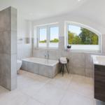 Bad mit Badewanne, Dusche und Waschbecken. Fenster mit Blick auf Bäume.