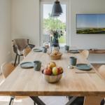 Essbereich mit Holztisch, Stühlen und Obst. Fernseher an der Wand. Blick auf Garten.