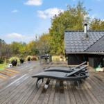 Wooden terrace with loungers, table, and chairs. Background: forest and house with roof.