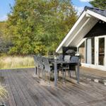 Deck with table and chairs in front of a house with glass doors.