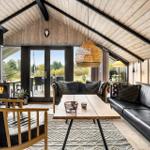 Living room with fireplace, sofa, and table. Wooden ceiling and large windows.