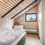 Bedroom with wooden walls, sloped ceiling, and window with view of trees.