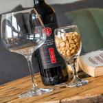 Ein Weinglas, eine Flasche Rotwein und eine Gläser mit Erdnüssen stehen auf einem Holztisch.