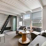 Wohnraum mit Sofa, Sitzgelegenheit und Tisch. Fenster und Dachschrägen sichtbar.