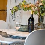 Esstisch mit Platz für zwei, Weinglas und Flasche, Blumenarrangement im Hintergrund.