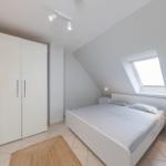 Schlafzimmer mit Dachschrägen, Dachfenster, weißem Bett und Kleiderschrank.