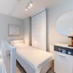 Ein Schlafzimmer mit Bett, Schrank und Wandspiegel. An der Wand hängt ein Bild.