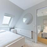 Schlafzimmer mit Dachfenster und Spiegel. Nebenraum mit Bett und Wandbild.