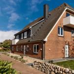 Ein zweistöckiges Haus mit Backsteinfassade und Balkon unter blauem Himmel.