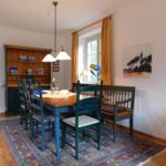 Esszimmer mit Holztisch, Stühlen und Regal. Fenster mit Vorhängen und Teppich.