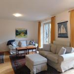 Wohnzimmer mit zwei Sofas, Tisch, Teppich und Fenstern mit Vorhängen.