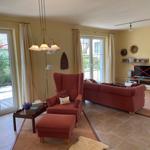 Wohnzimmer mit rotem Sofa, Sessel und Terrassentür. Fernseher auf Holzregal.