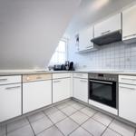 Küche mit weißen Schränken, Edelstahlgeräten und Fliesenboden.