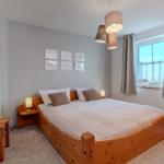 Schlafzimmer mit Holzbett, Fenster und Spiegel.