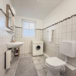 Badezimmer mit Waschmaschine, WC und Spiegel an der Wand.