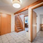 Eingangsbereich mit Holztreppe und Tür. Blick in Wohn- und Schlafzimmer.
