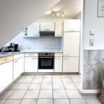 Küche mit weißen Schränken, Edelstahlspüle und integriertem Backofen.