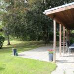 Patio with table and chairs under roof, surrounded by grass and trees.