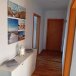 Flur mit Holzboden, weißen Wänden und Wandbildern mit Strandmotiven.