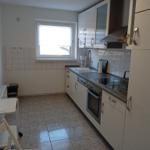 Küche mit weißen Schränken, Herd, Spüle und Fenster.