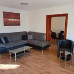 Wohnzimmer mit Sofa, Sesseln und Glas-Tisch. Durchgang zum Essbereich.