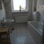 Badezimmer mit Badewanne, Waschbecken und Fenster mit Jalousie.