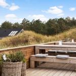 Wooden terrace with benches and cushions, view of forest and sky.
