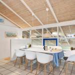 Dining area with white table and chairs under wooden ceiling with white beams.