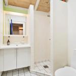 Bathroom with shower, sink, and toilet. Wooden ceiling and white tiles.