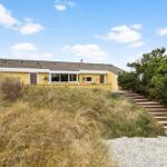 Yellow house with wooden steps and grassy slope under blue sky.