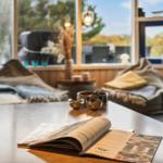 A table with an open magazine. In the background are two seats and large windows.