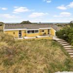 A yellow house with a terrace on dunes, view of the sea.