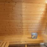 Sauna mit Holzwand und Sitzbank. Auf der Bank steht ein Metalleimer.