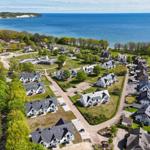 Aerial view of coastal residential area with houses, greenery, and sea in background.