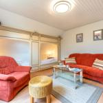 Wohnzimmer mit rotem Sofa und Sessel, Glas-Tisch und zwei Schlafnischen.