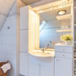 Badezimmer mit Waschbecken, Spiegel und Regalen. Dachneigung und weiße Fliesen.